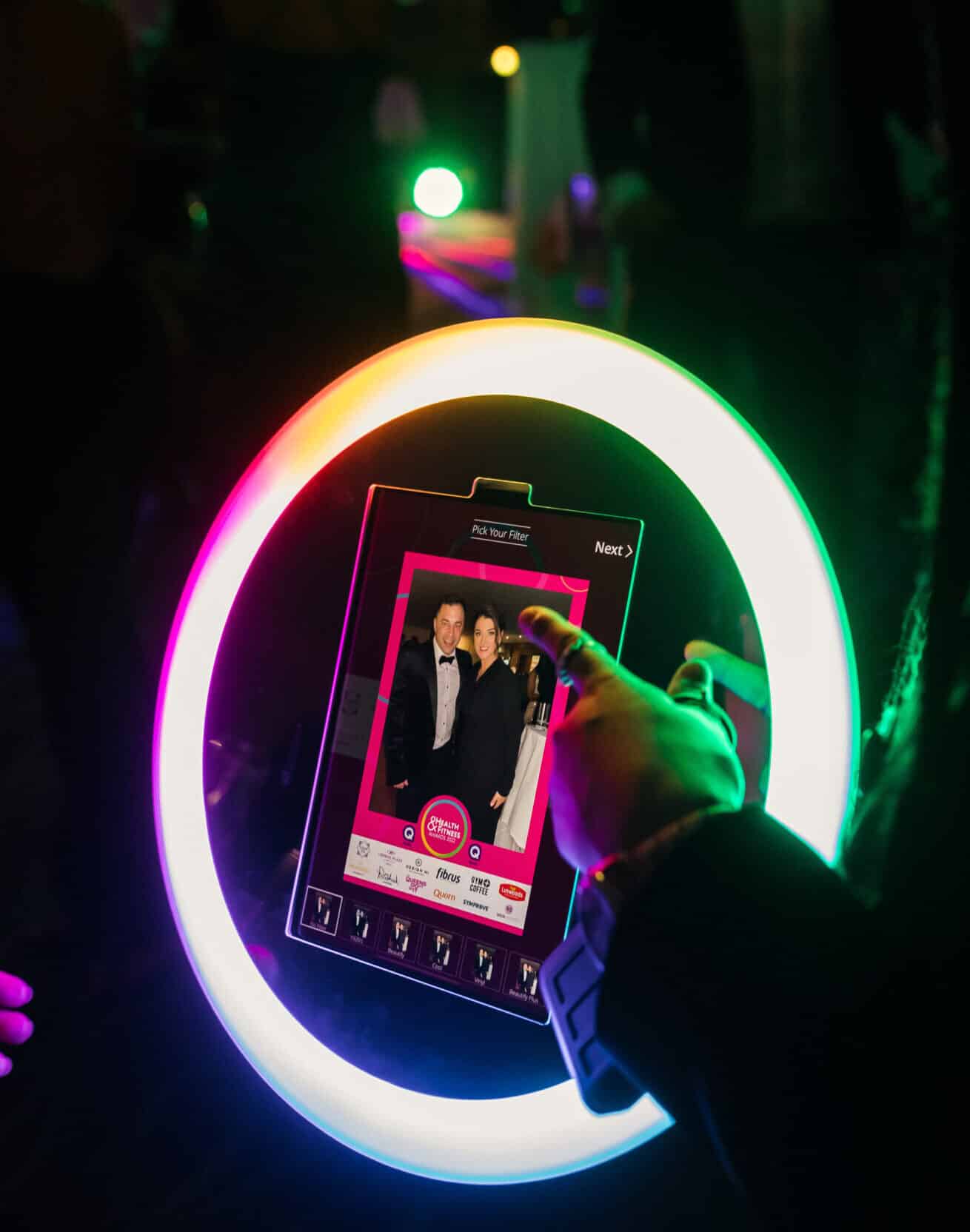 A group of people smiling and posing for a picture in a photo booth at an event, holding a large, custom-branded frame.