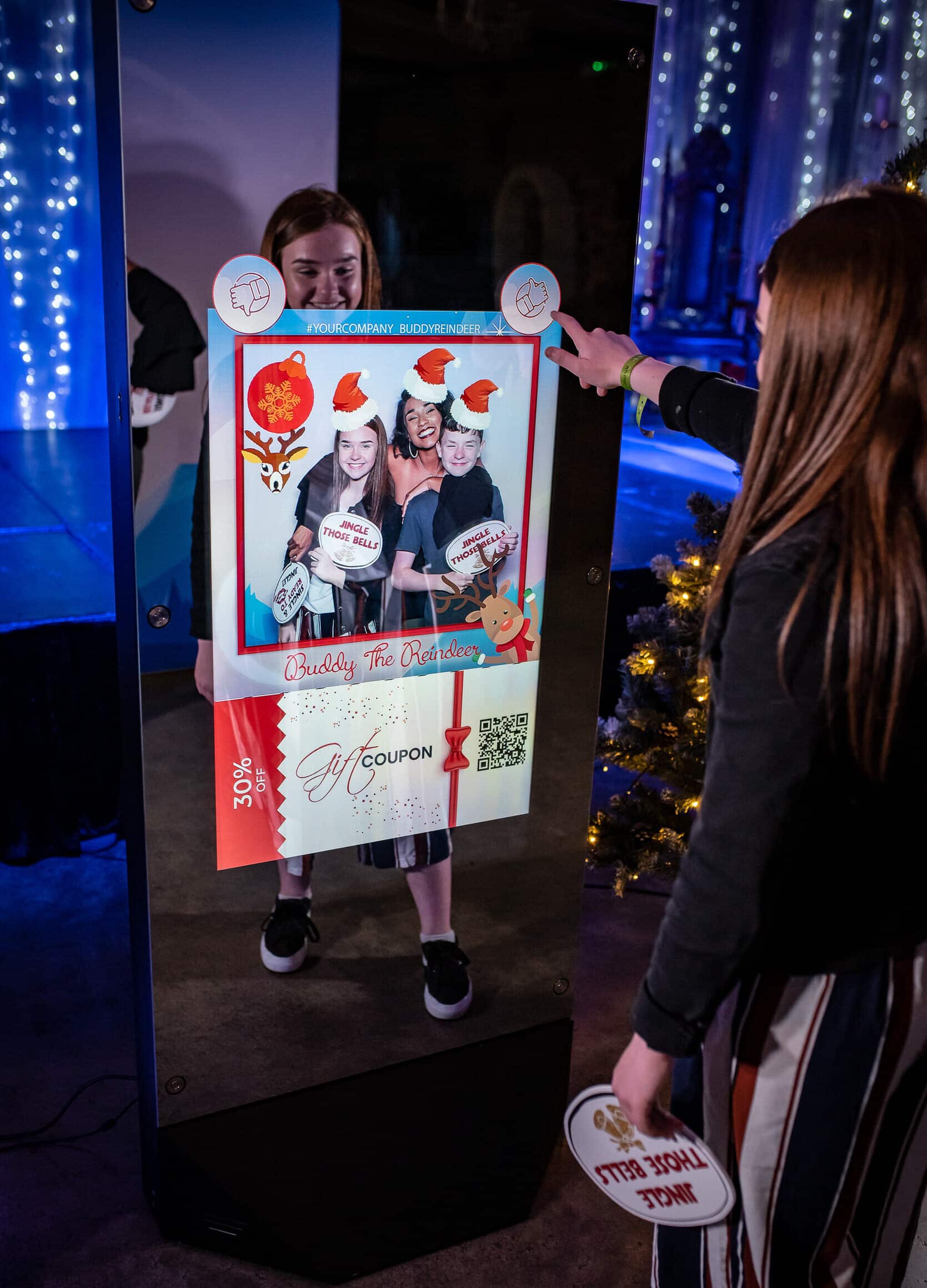 Two women in formal dresses smiling and posing for a picture in a photo booth at an event.