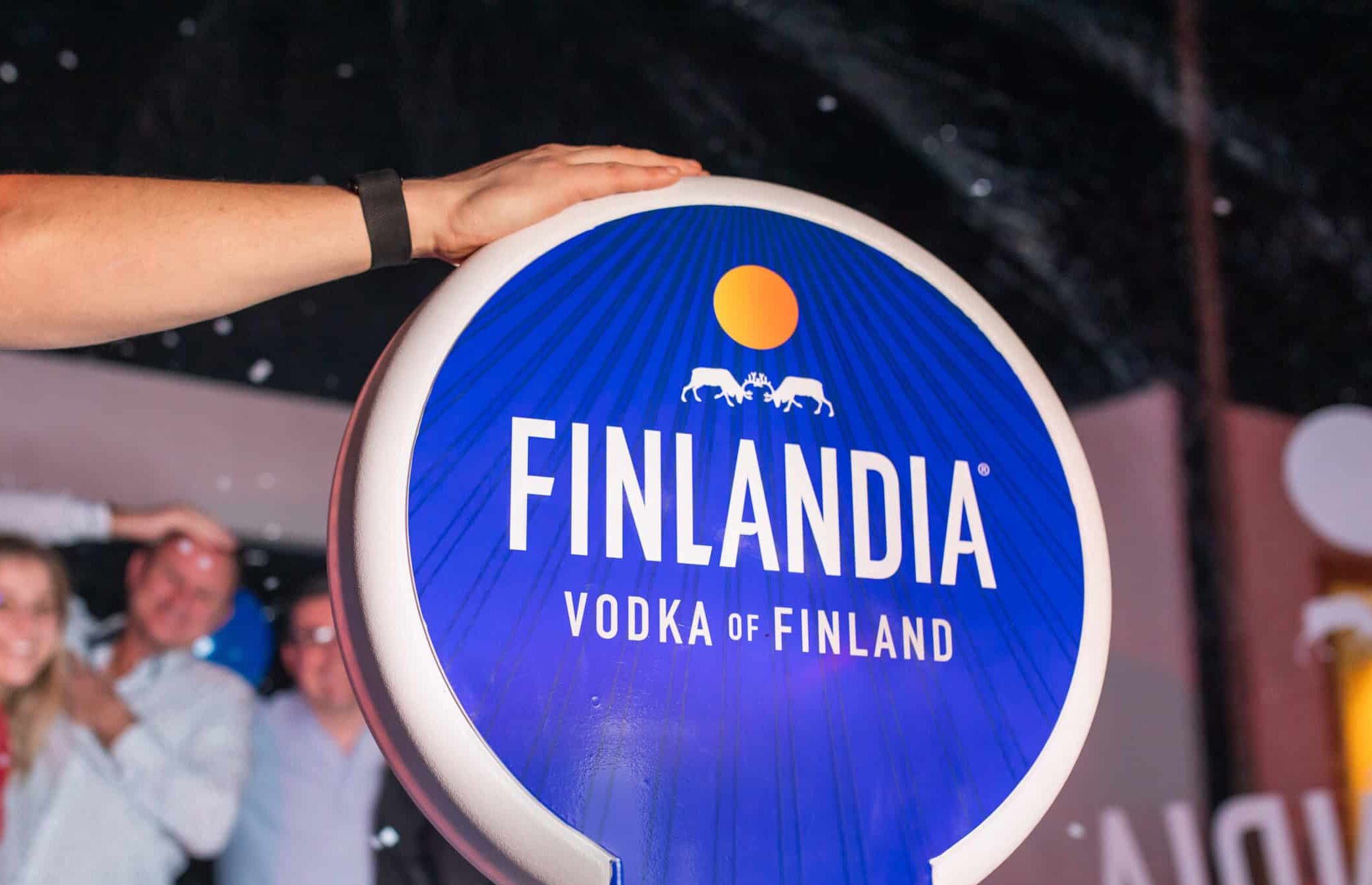 Two women in formal dresses smiling and posing for a picture in a photo booth at a corporate event.