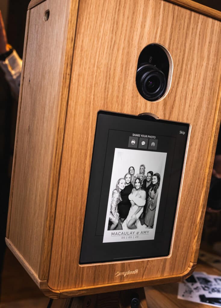 A group of people smiling and posing for a picture in a photo booth, holding various props including hats and a sign.