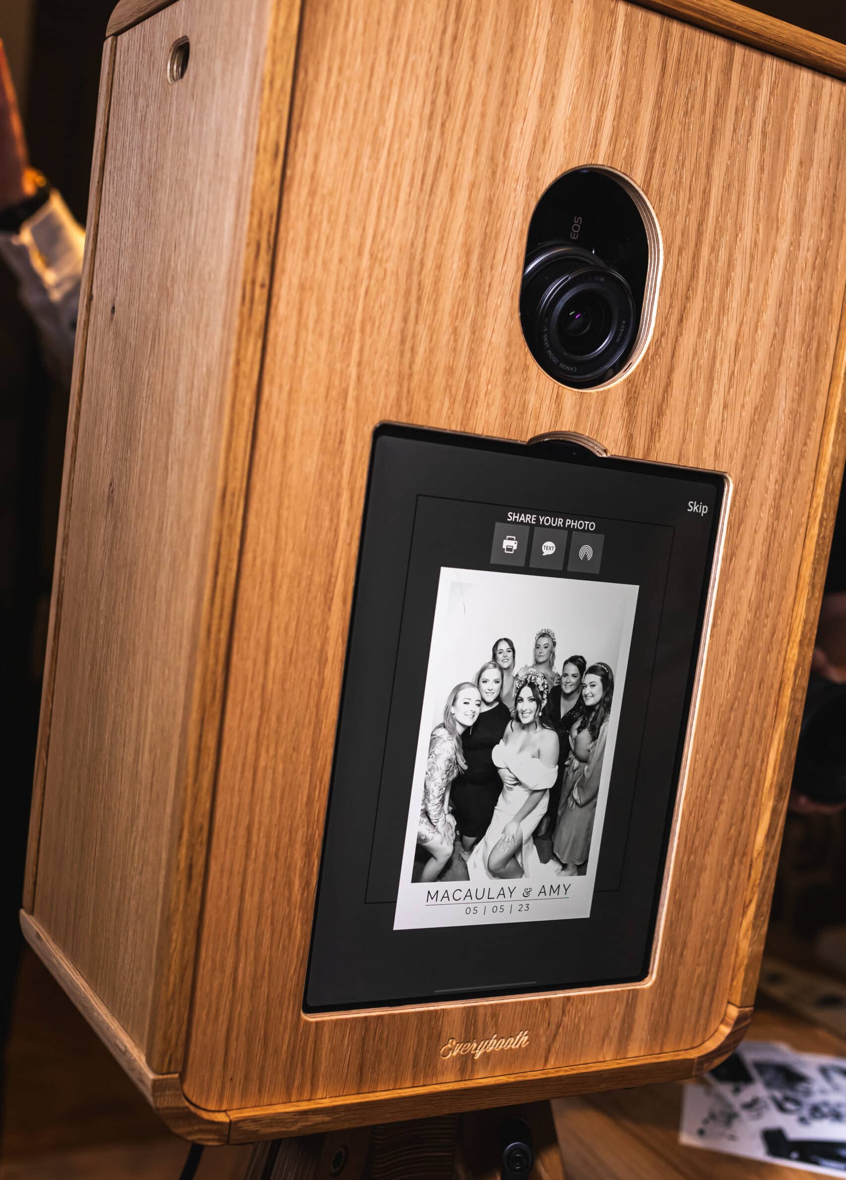 A group of people smiling and posing for a picture in a photo booth, holding various props including hats and a sign.