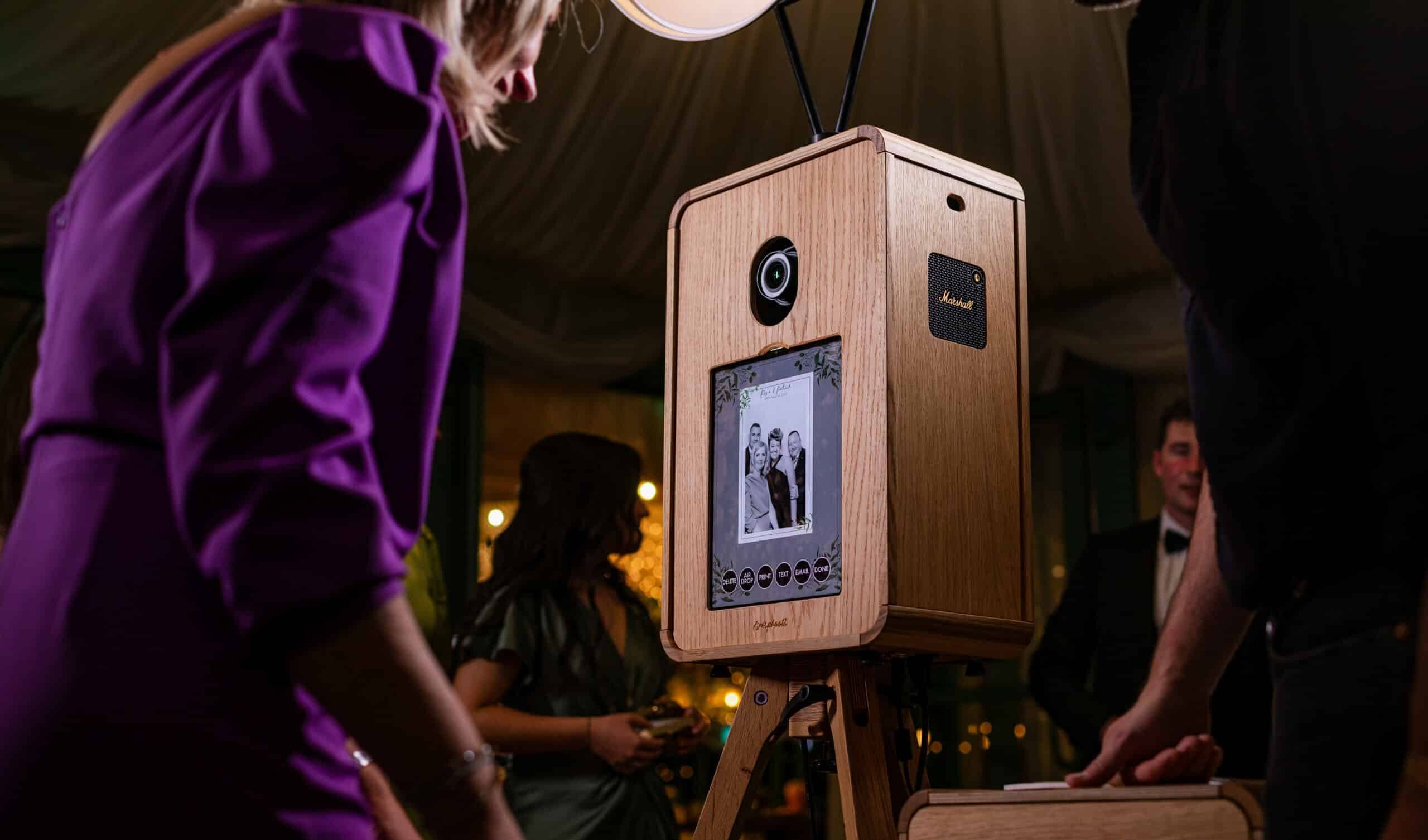 Two women smiling and posing for a picture in a photo booth, holding various props including a hat and a star-shaped sign.