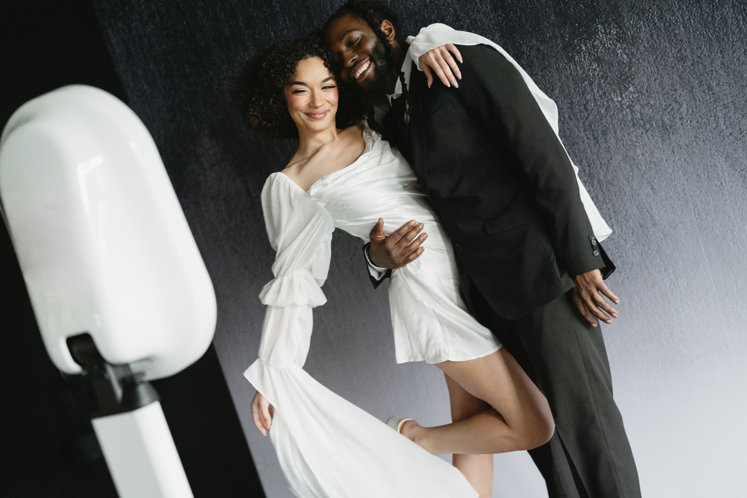 A couple smiling and posing for a picture at their wedding, holding a sign that says "Cheers to Mr. and Mrs."