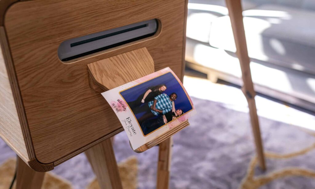 A couple smiling and posing for a picture in a photo booth at their wedding, with a custom backdrop featuring their names.