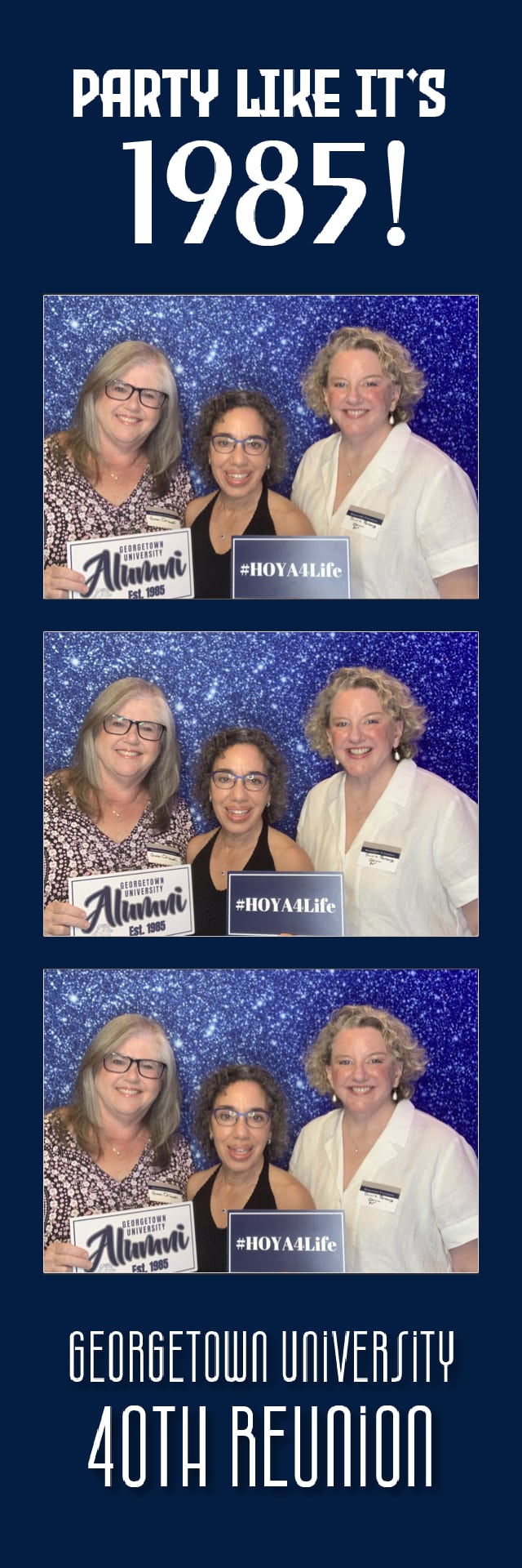 Two women smiling and posing for a picture at a university reunion event, with one holding a cup and the other holding a small sign.