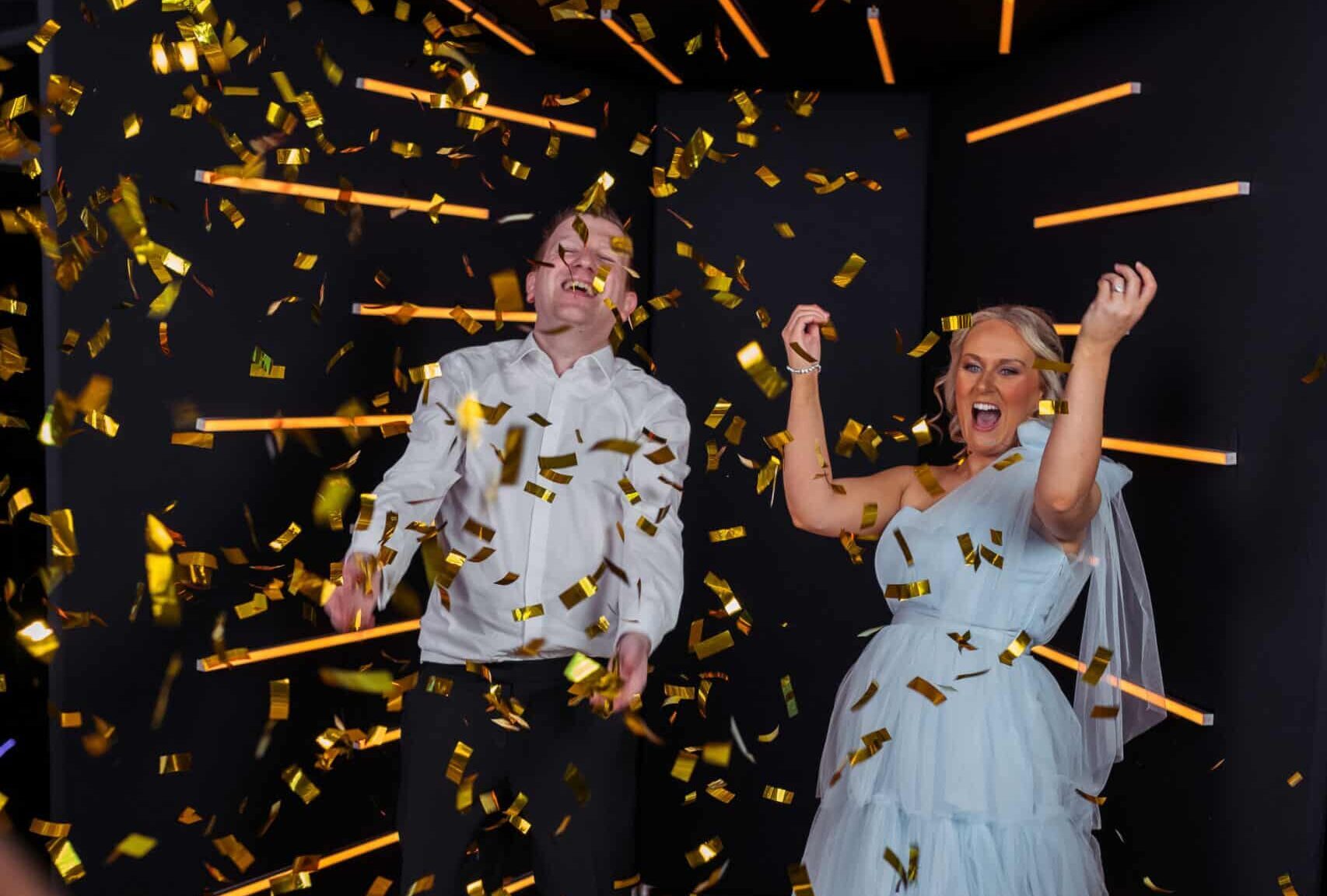 Two people striking a dramatic pose inside a "Vogue Booth" with a bright, professional lighting setup and a modern white backdrop.