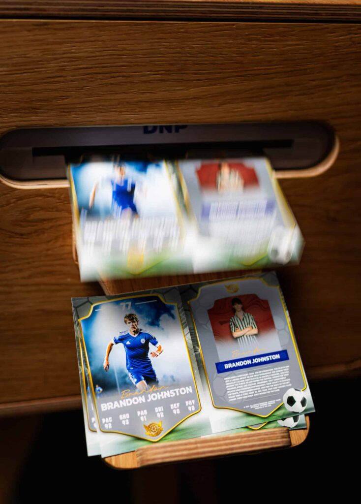 A group of people smiling at a camera inside a photo booth with a sleek, white background and cutsom trading cards..