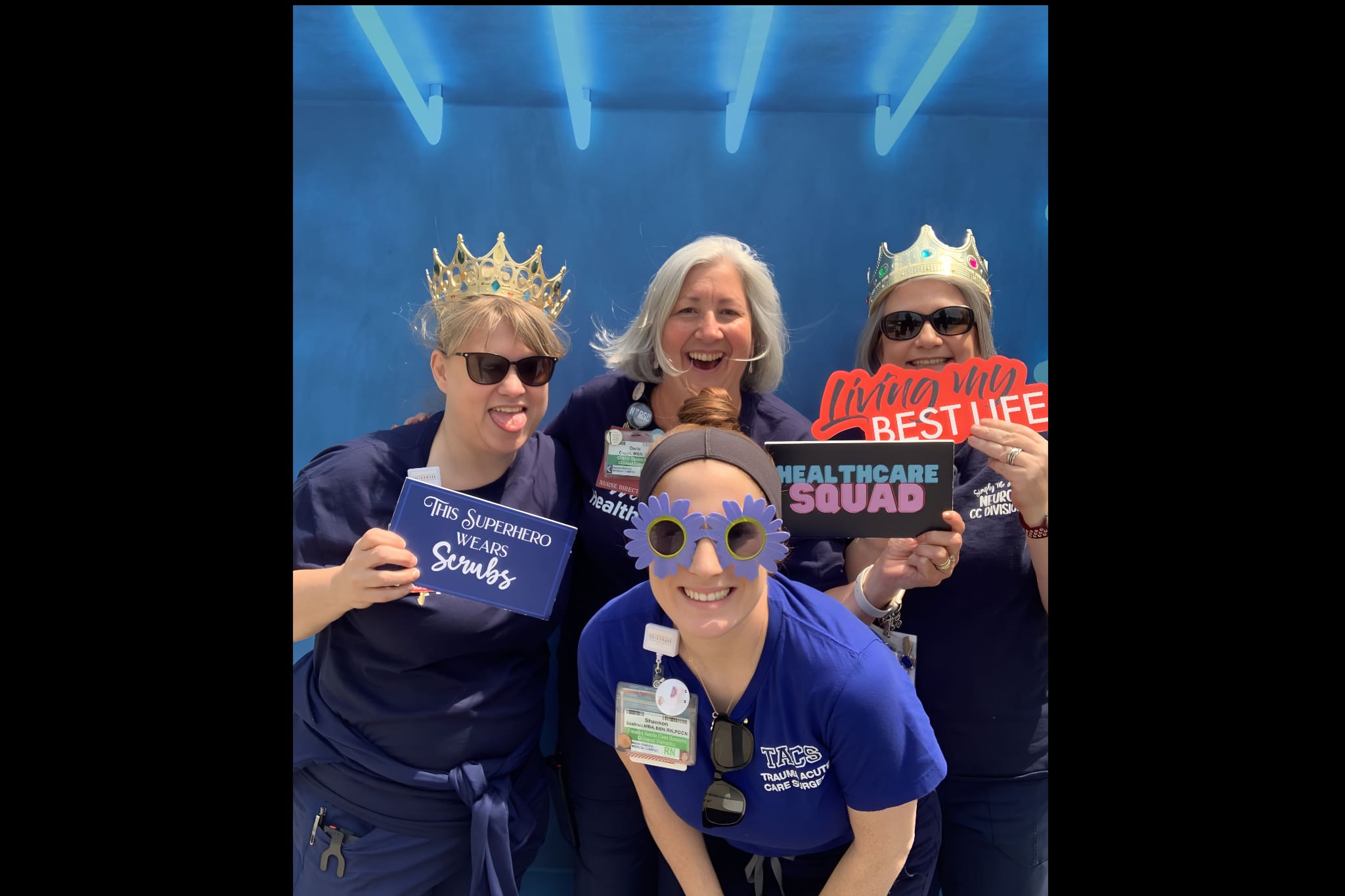 Hospital workers holding photo booth props and posing in front of a blue backdrop. They are wearing funny glasses having a good time for the photo booth.