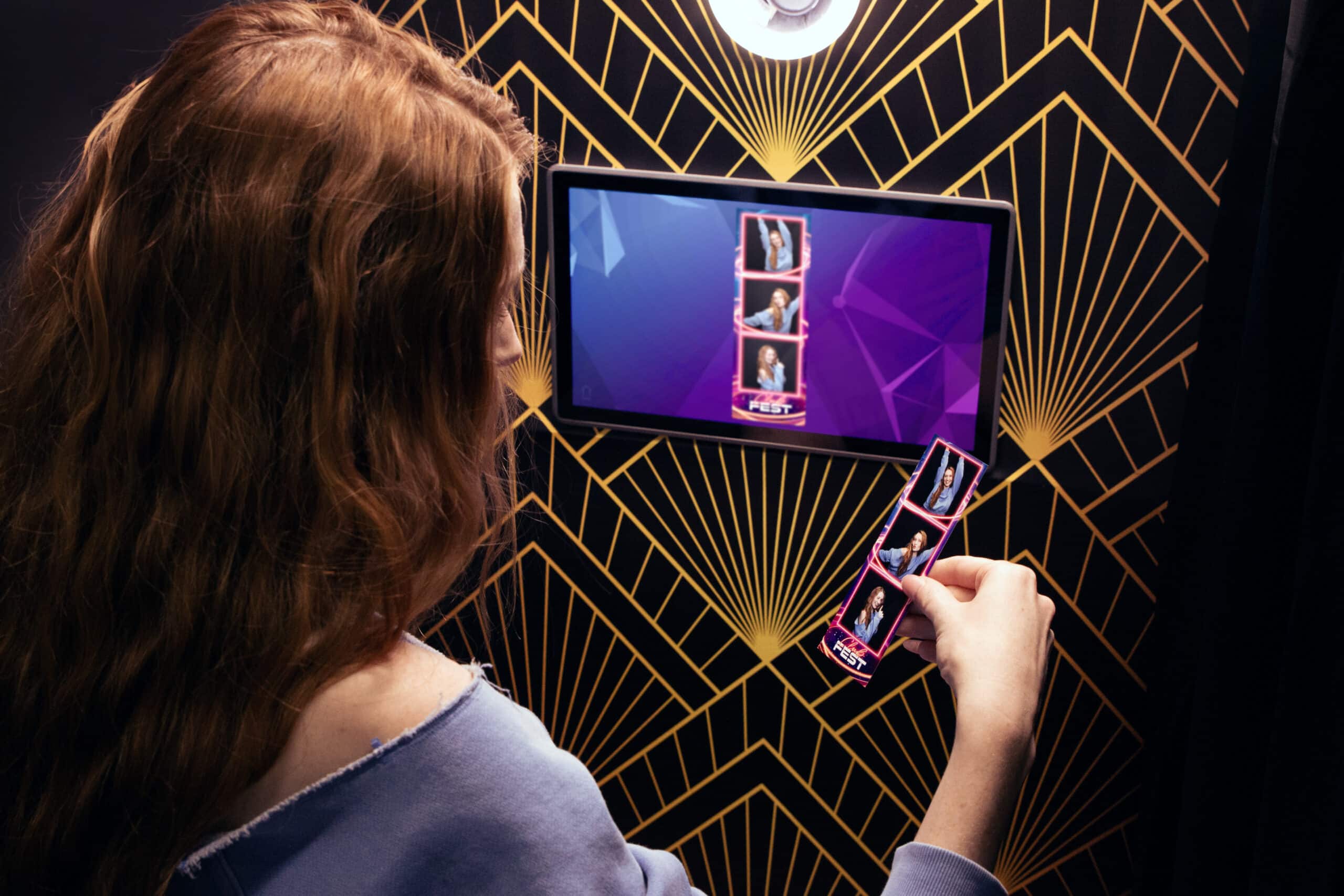 A sleek, modern enclosed photo booth with a black exterior and a red curtain backdrop, ready for guests to take photos.
