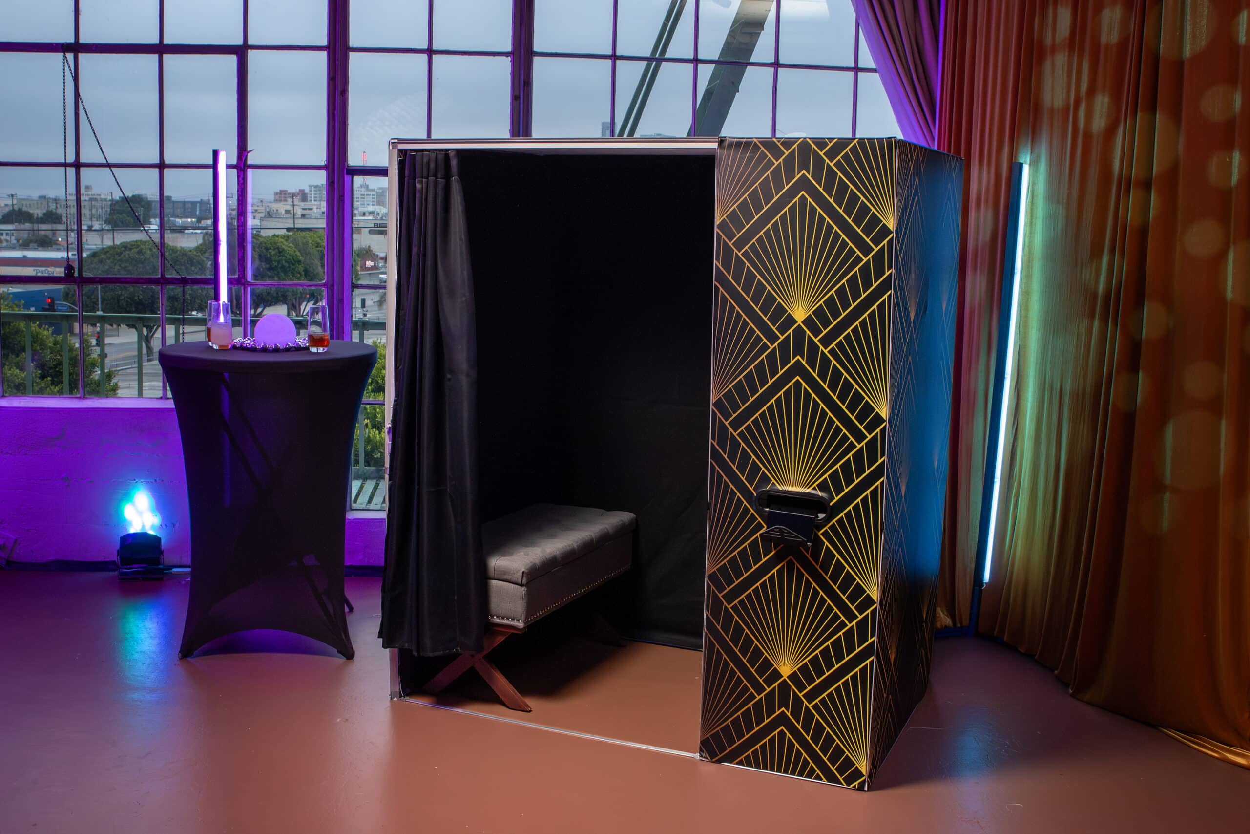 A group of people smiling and posing for a picture inside a black enclosed photo booth with a red curtain backdrop.
