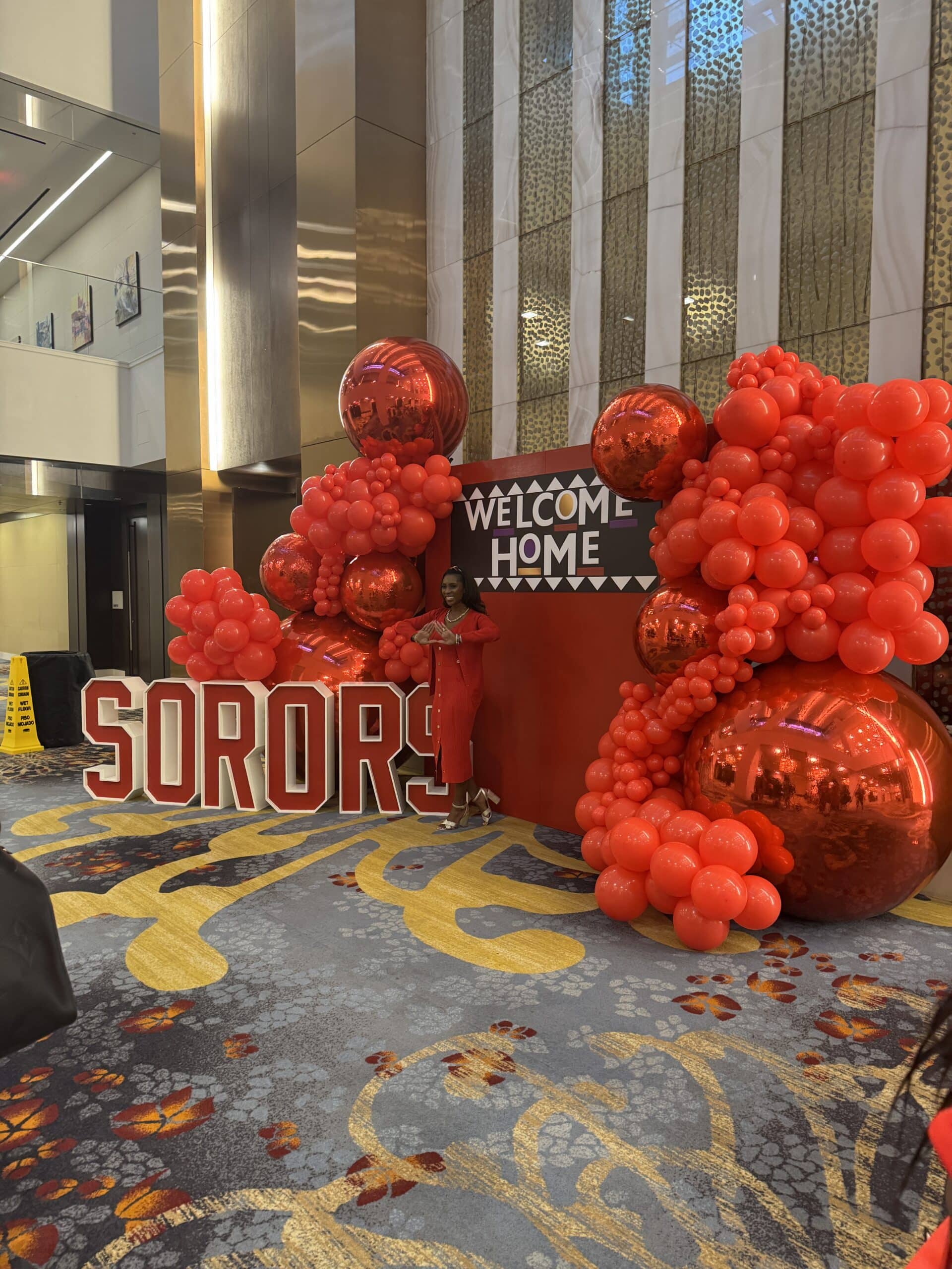 Two women posing for a photo at a national convention's photo experience, holding a custom prop with a logo.