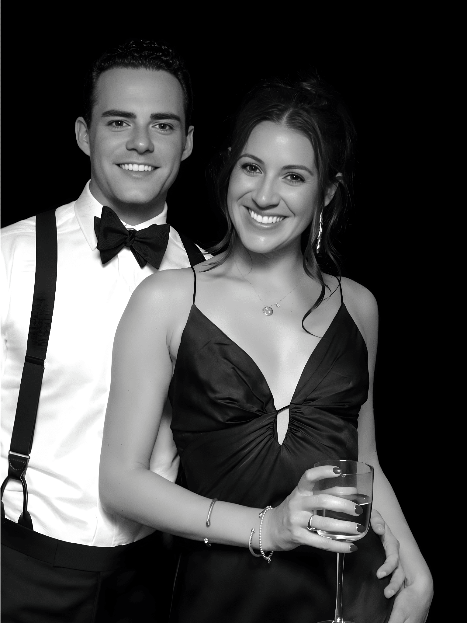 Couple in elegant attire posing together, smiling, with a glass of drink, showcasing a glamorous photo booth experience.