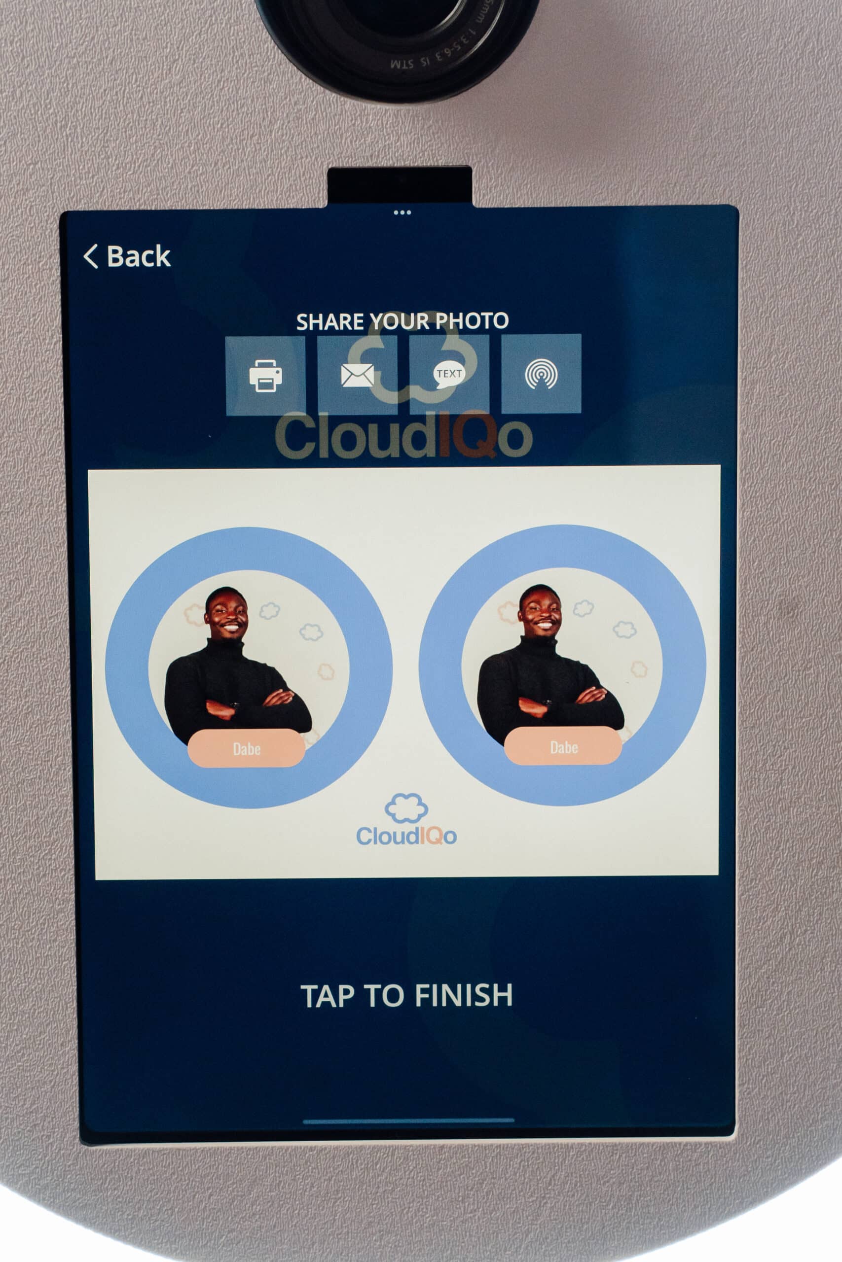 Screen display of a photo booth interface featuring two identical images of a smiling man named Dabe, with options to share the photo via email or text, branded with CloudIQ logo, emphasizing user engagement at events.