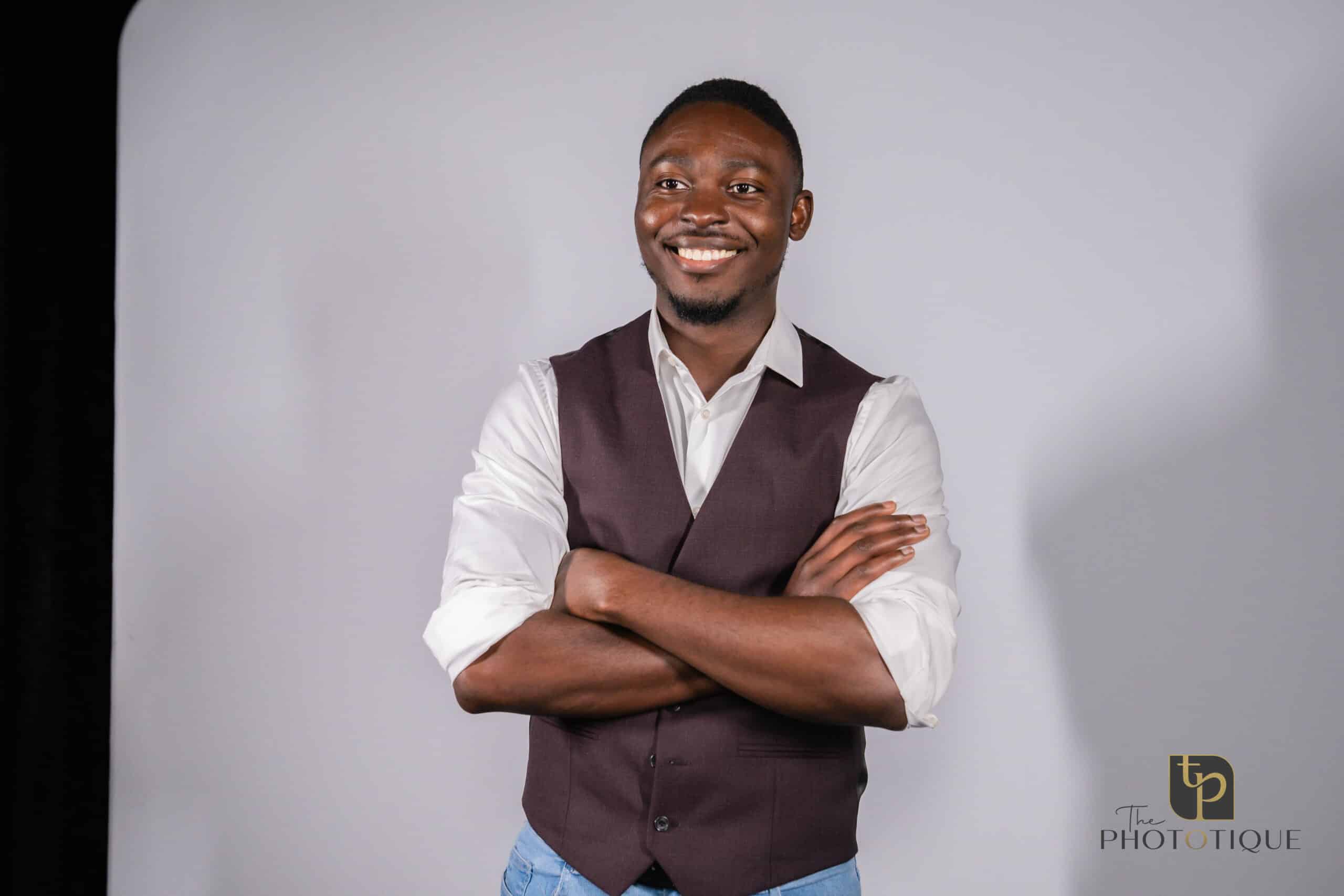 Smiling man in a vest and shirt posing confidently with arms crossed against a neutral backdrop, representing The Phototique's headshot booth experience for events.