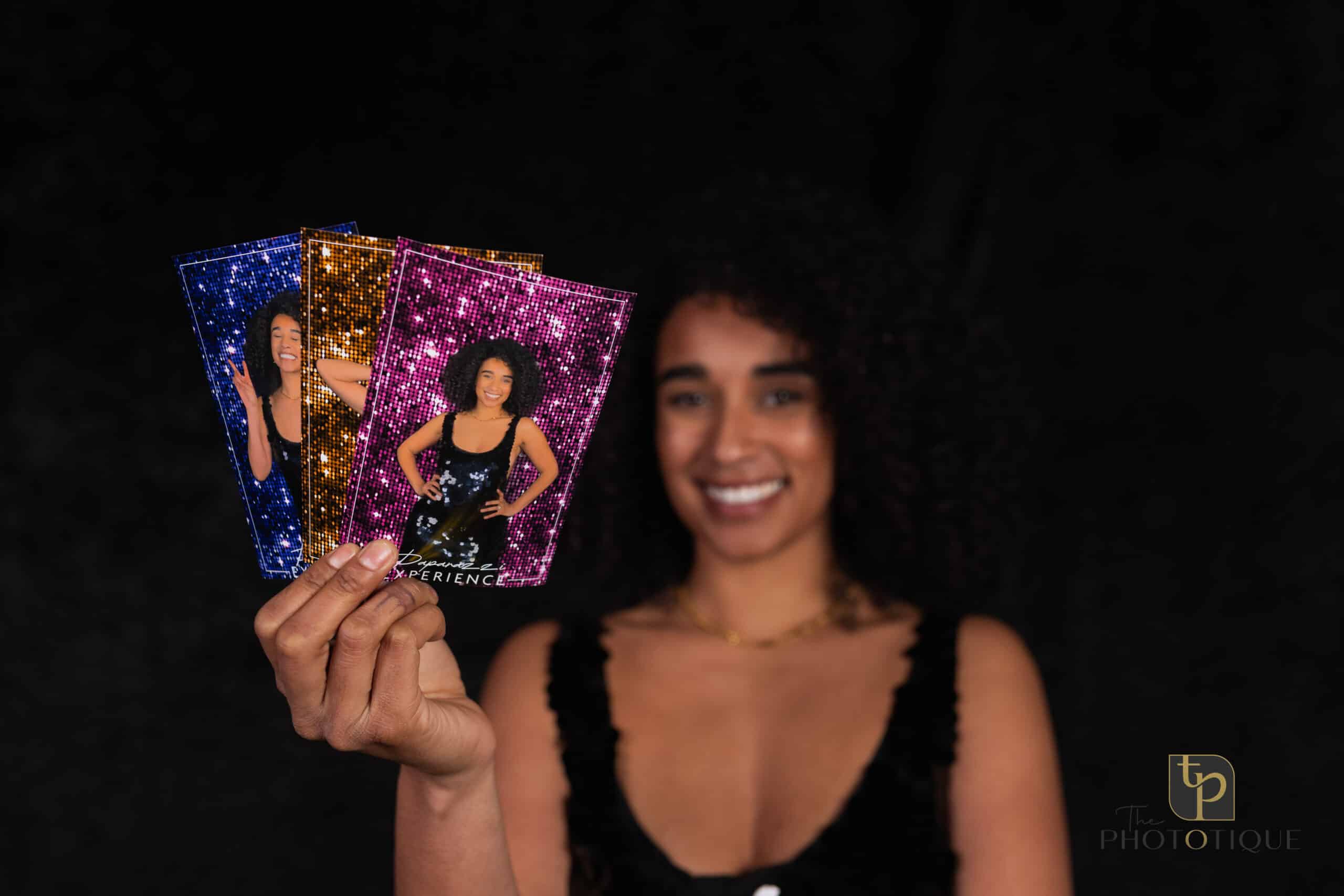 Smiling woman holding colorful photo booth prints featuring her image, showcasing The Phototique's immersive photo booth experience.