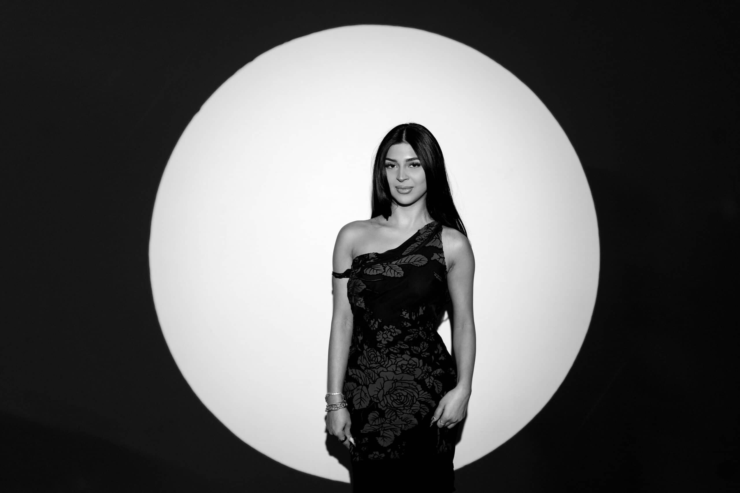 Woman posing in elegant black dress against a large circular backdrop, showcasing a glamorous photo booth experience.