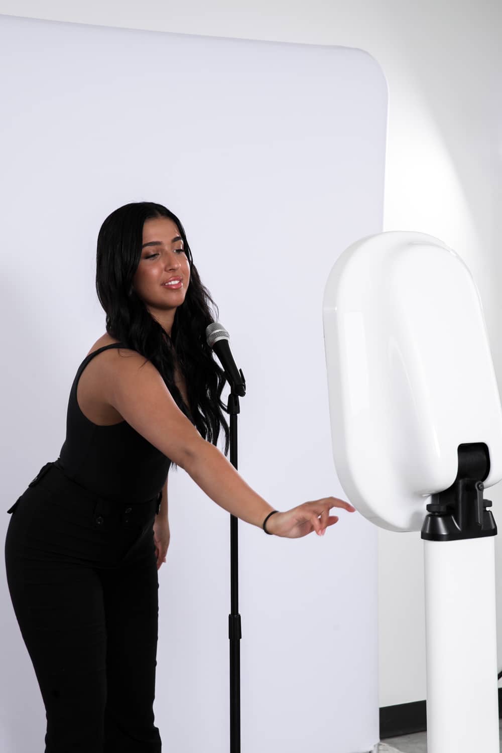 Young woman interacting with a video booth setup, microphone in hand, against a plain backdrop, showcasing The Phototique's immersive photo booth experience for events.