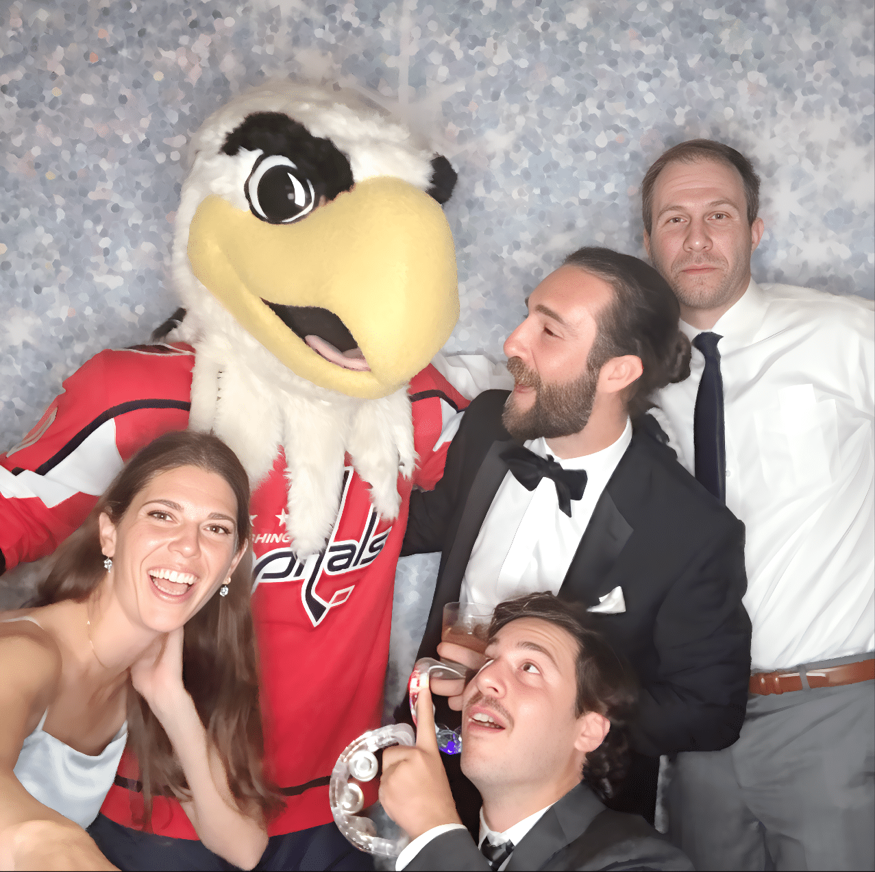 Group of guests posing joyfully in a photo booth with a mascot in a Washington Capitals jersey, featuring playful expressions and festive attire, highlighting an engaging event experience.