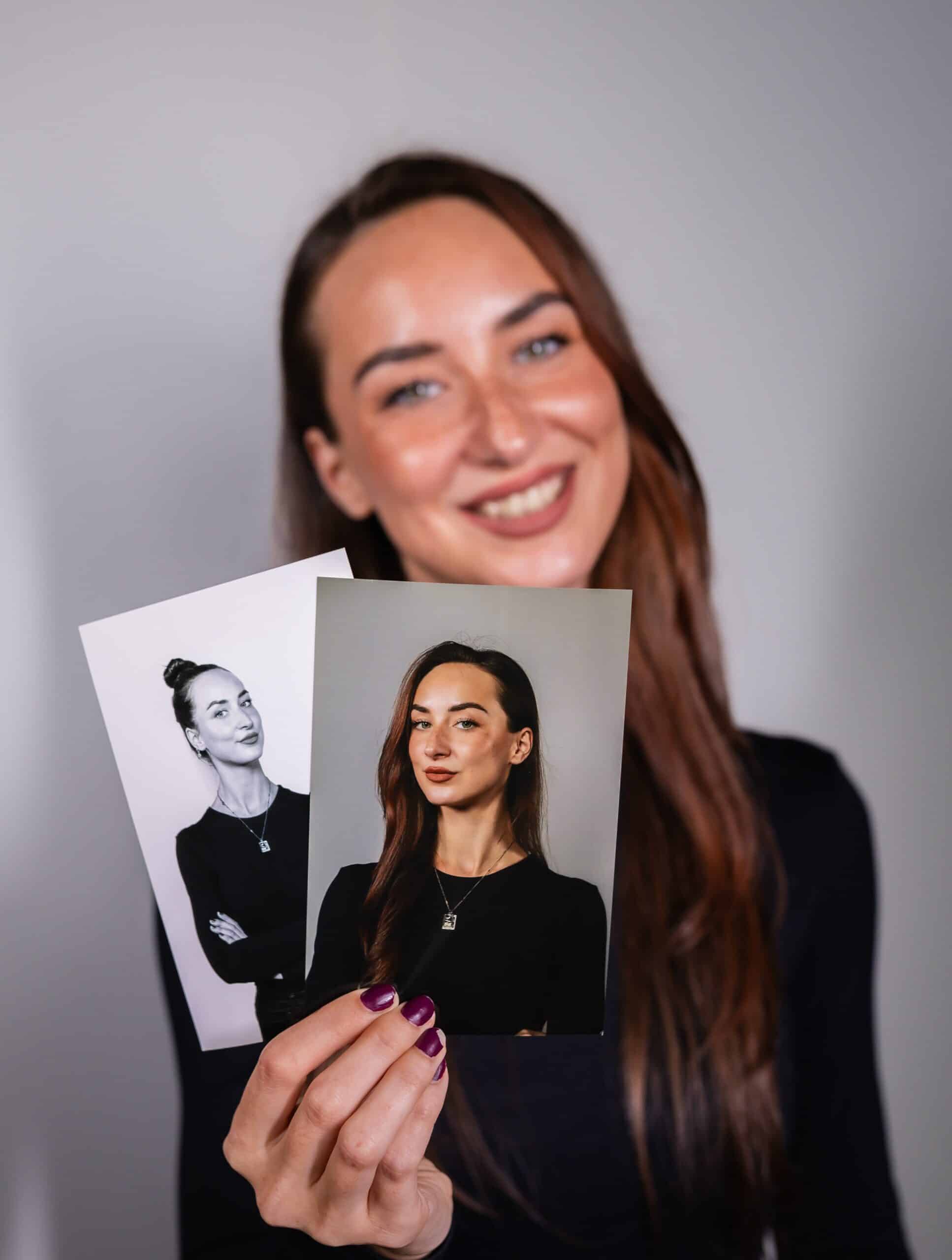 Woman holding two printed photos showcasing custom keepsakes from a branded event station, smiling and dressed in black, with a neutral background.