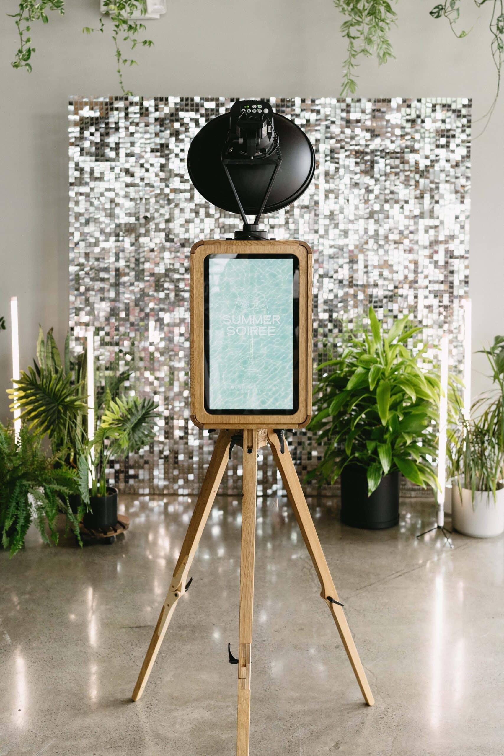 Photo booth setup featuring a sleek, modern design with a digital screen displaying "SUMMER SOIREE," surrounded by greenery and a sparkling backdrop, ideal for event branding and guest engagement in Washington, DC.