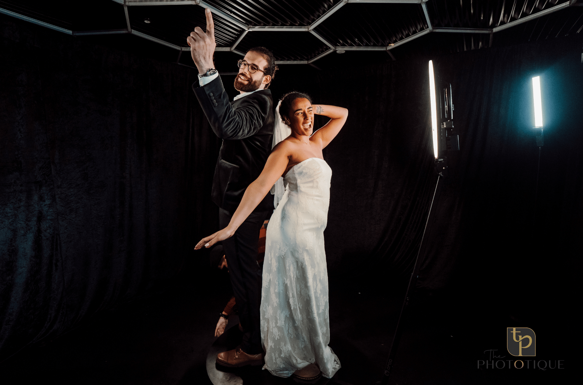 Couple posing playfully in a photo booth, highlighting a wedding theme with dramatic lighting, showcasing the immersive experience offered by Phototique.