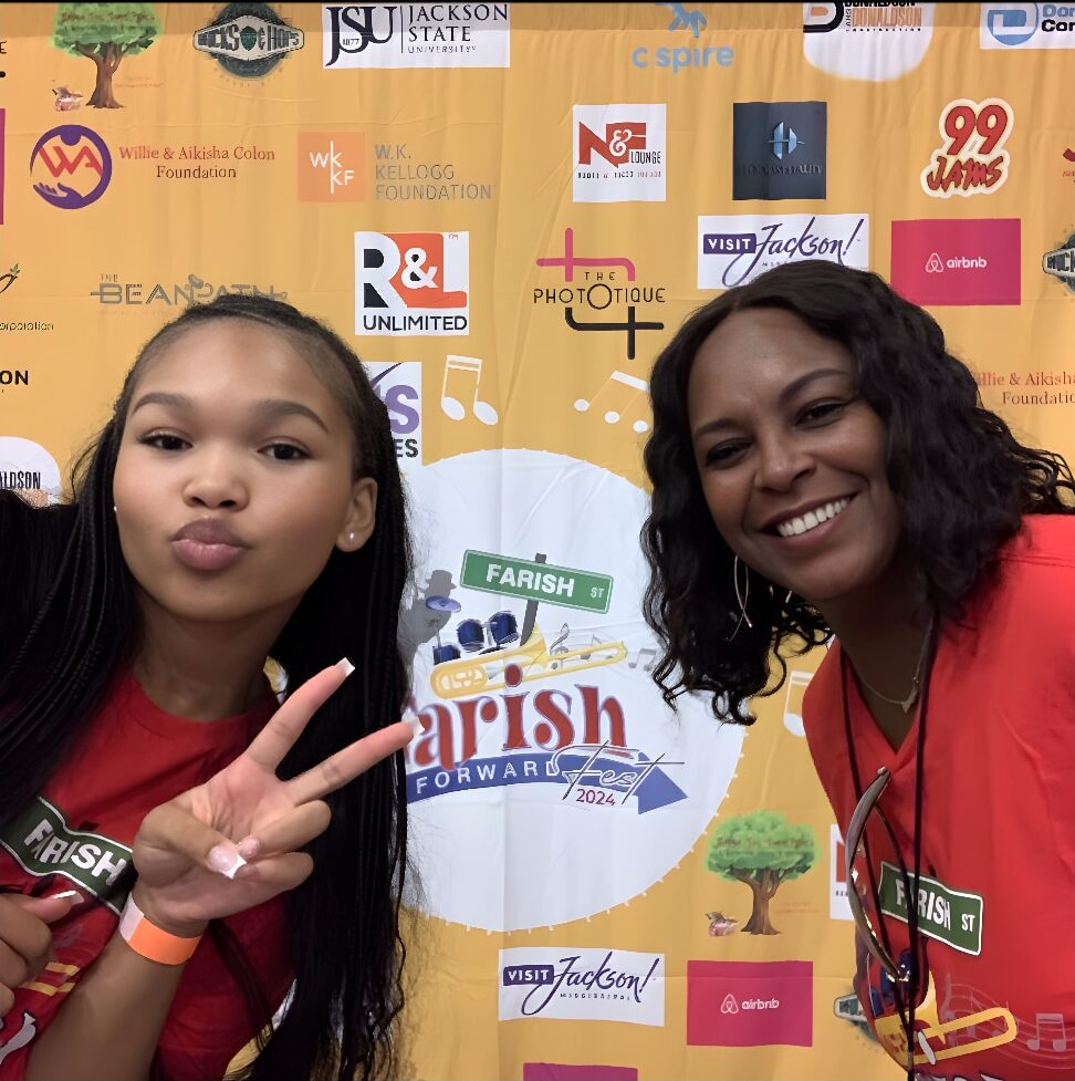 two ladies standing in front of a backdrop. One has her two fingers up in the peace sign gestrure