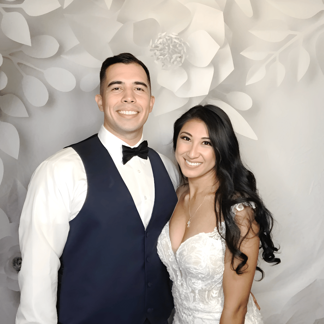 Couple posing happily in formal attire in front of a decorative floral backdrop, capturing a memorable moment at a wedding photo booth in the DC Metro Area.