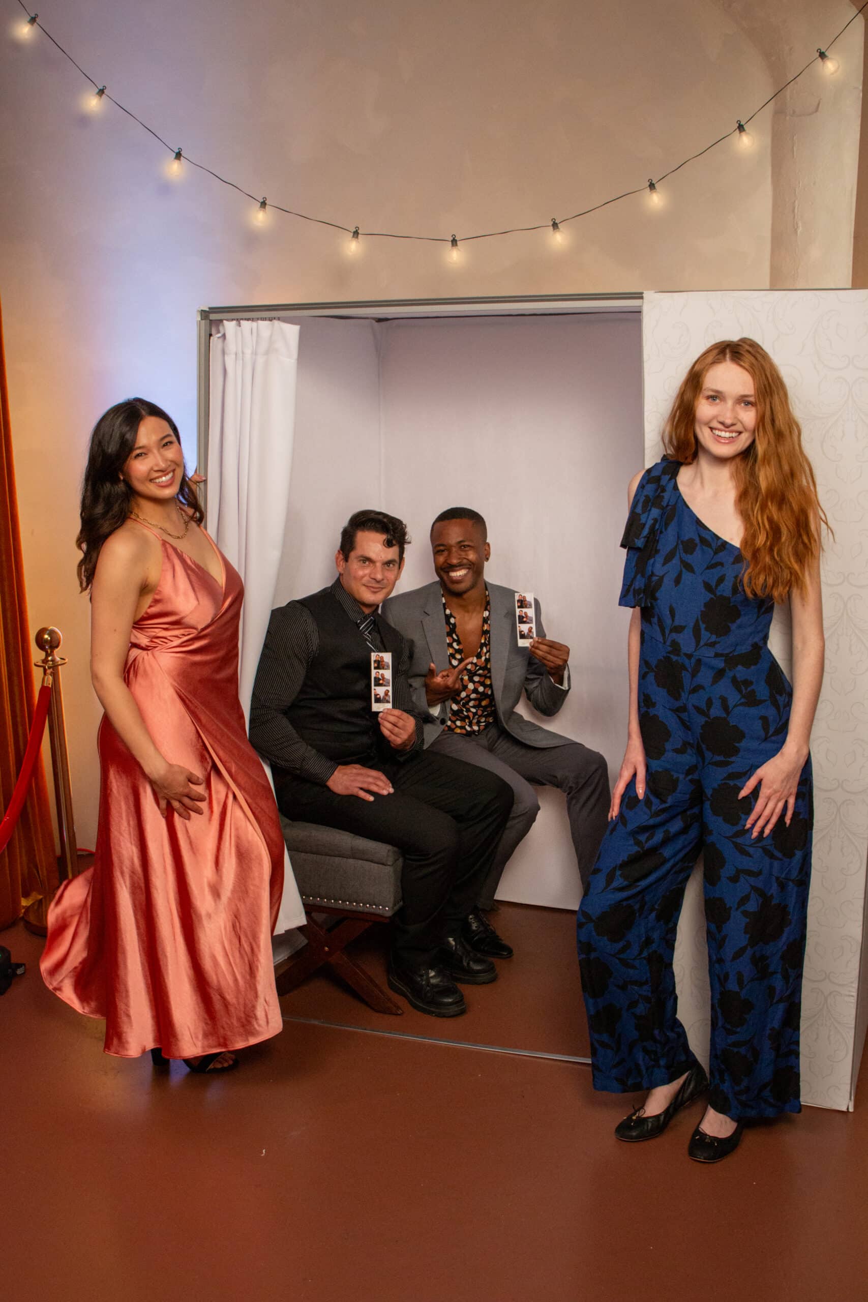 Group of four people posing in a photo booth, showcasing a stylish photo booth experience from The Phototique, with elegant attire and vibrant lighting, ideal for events like weddings and corporate gatherings.