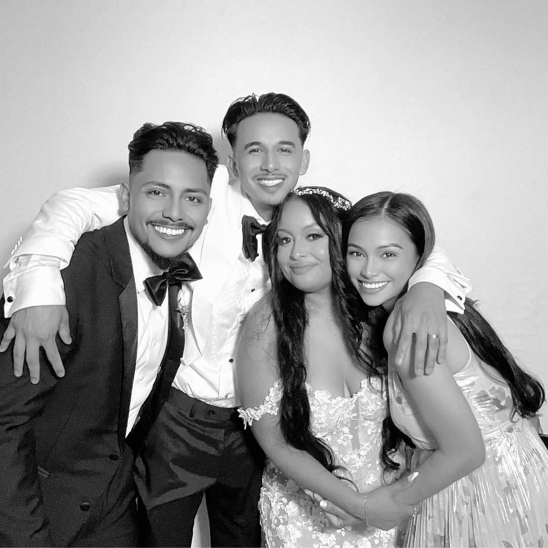 Group of four friends posing joyfully in a photo booth, dressed in formal attire, capturing a celebratory moment at a wedding reception.