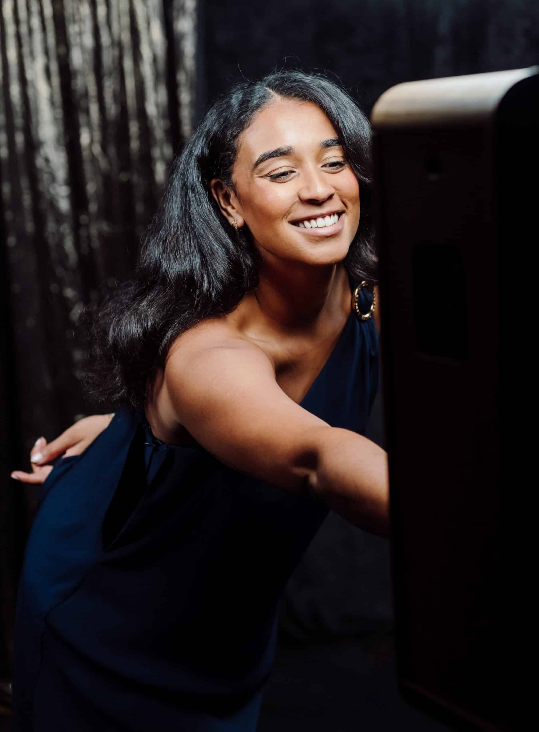 Smiling woman interacting with a GlamBot camera in a stylish event setting, capturing cinematic slow-motion video for a red-carpet experience.