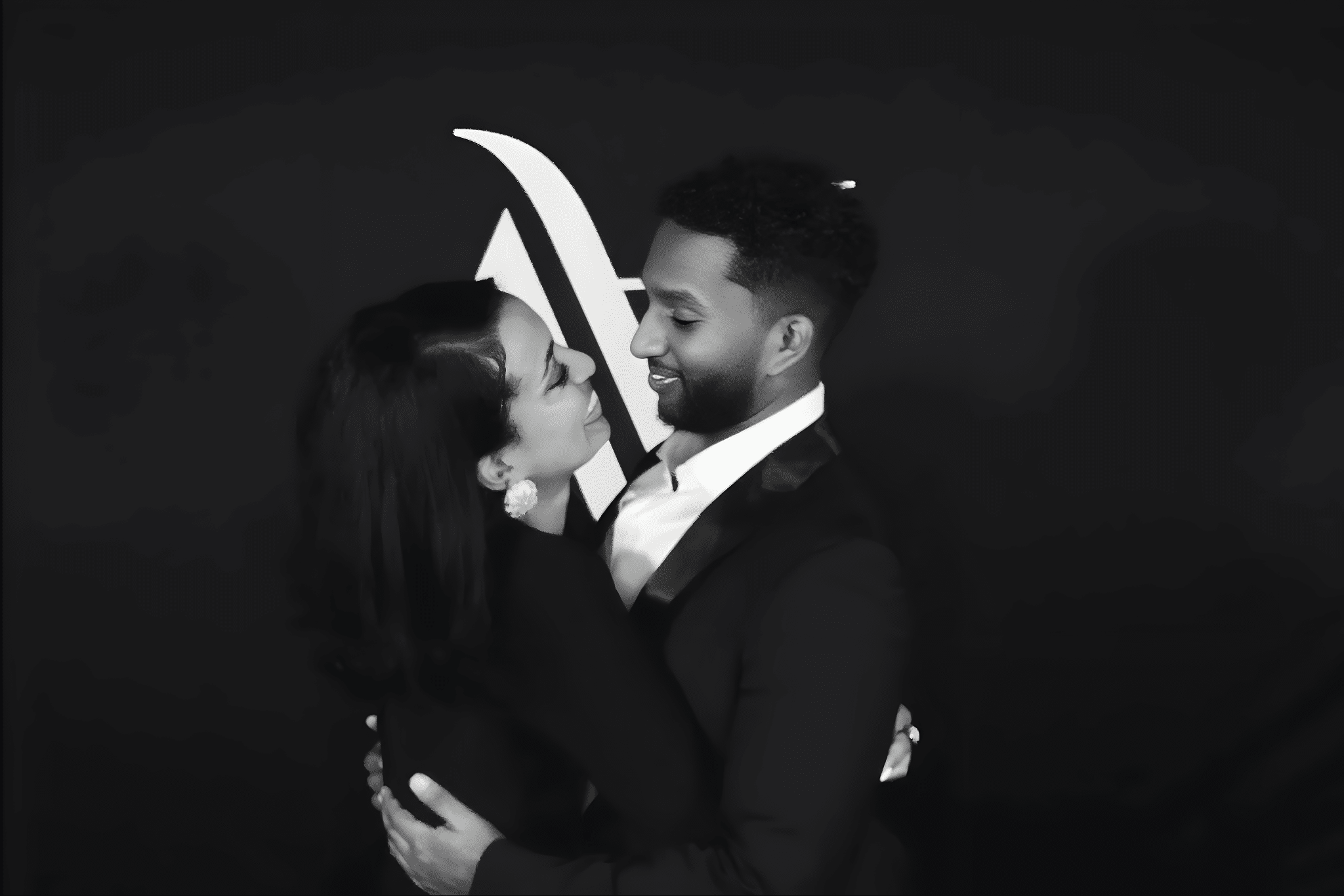 Couple embracing and smiling, dressed elegantly against a sleek black backdrop, capturing a glamorous moment in the Glam Noir photo booth experience.