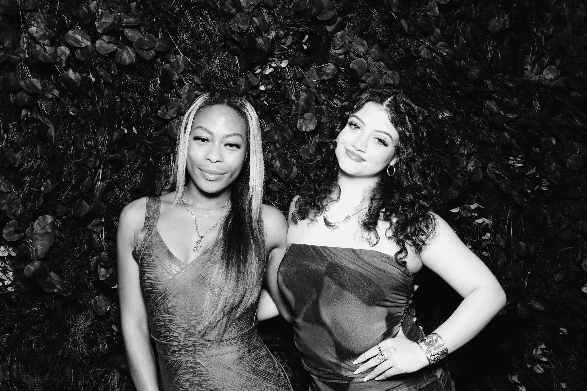 Two elegantly dressed women posing together in front of a lush green backdrop, capturing a glamorous moment suitable for red carpet events and brand activations.