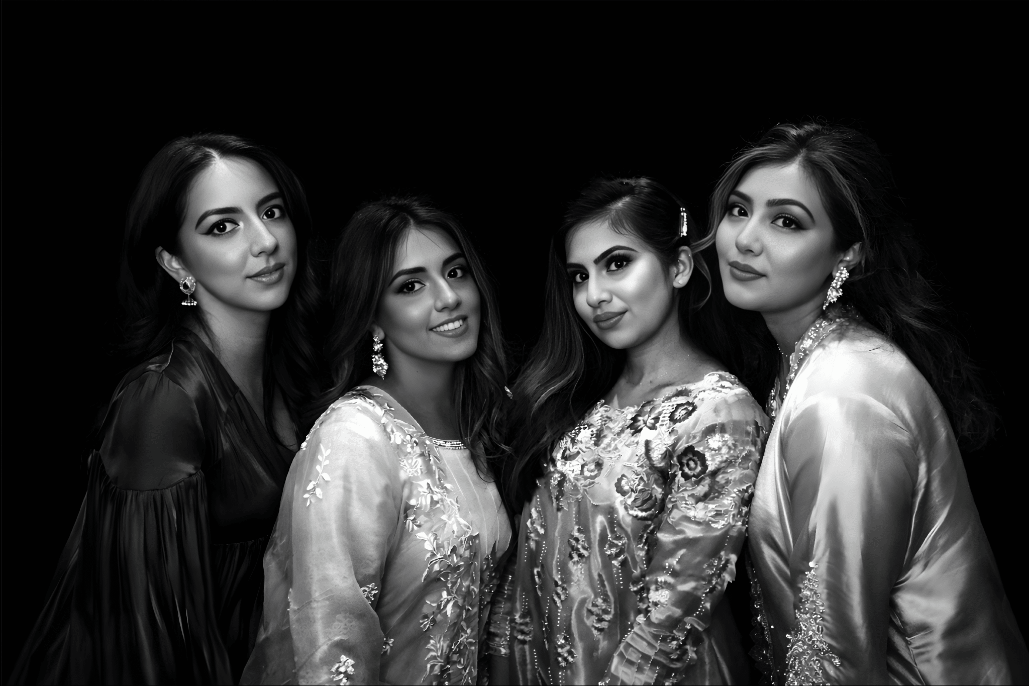 Four women in elegant attire posing together against a sleek black backdrop, showcasing the Glam Noir photo booth experience with a polished, editorial-quality finish.