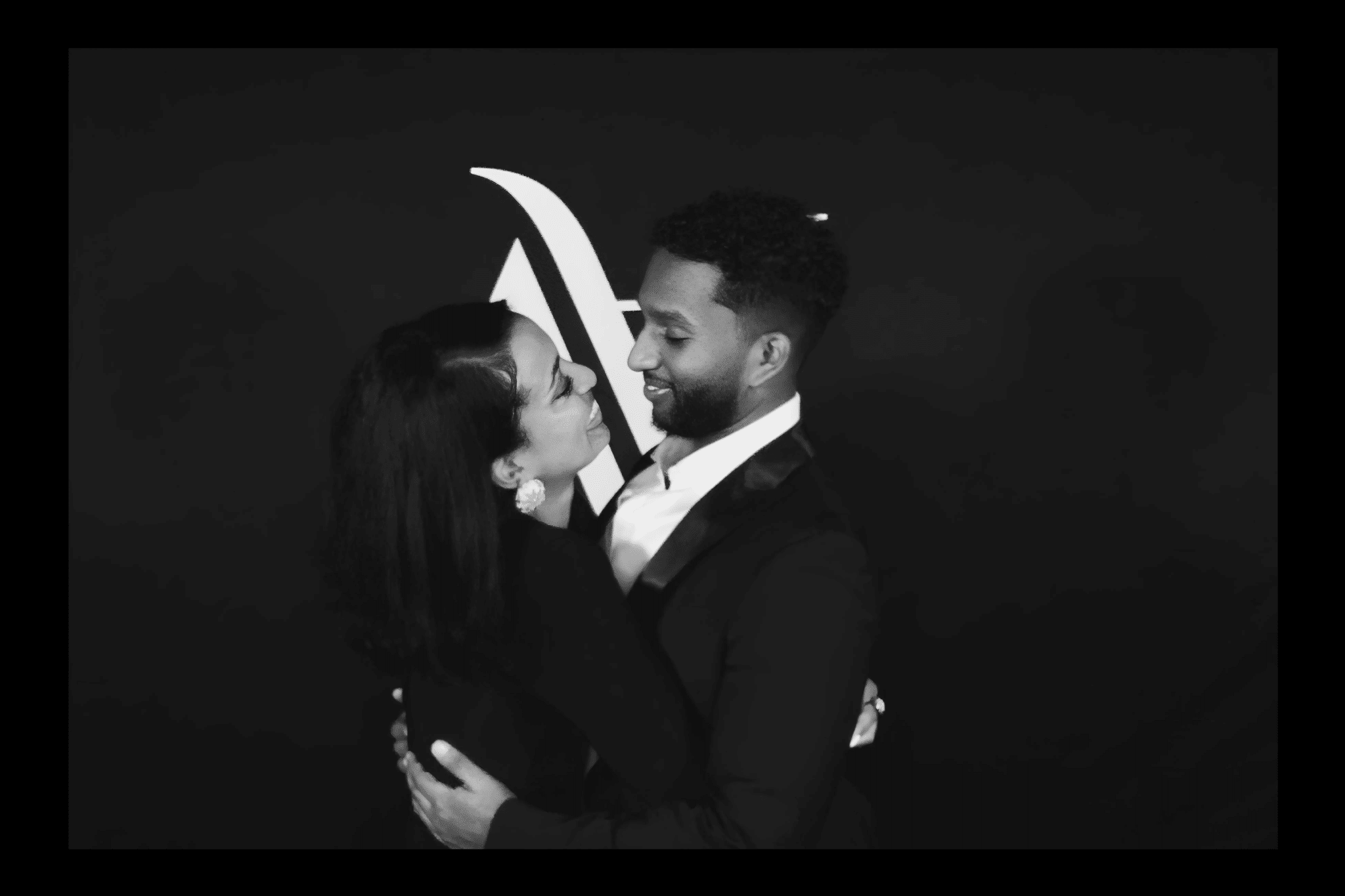 Couple embracing in glamorous attire against a dark backdrop, capturing a red-carpet moment, illustrating the cinematic slow-motion video experience offered by The Phototique for special events.