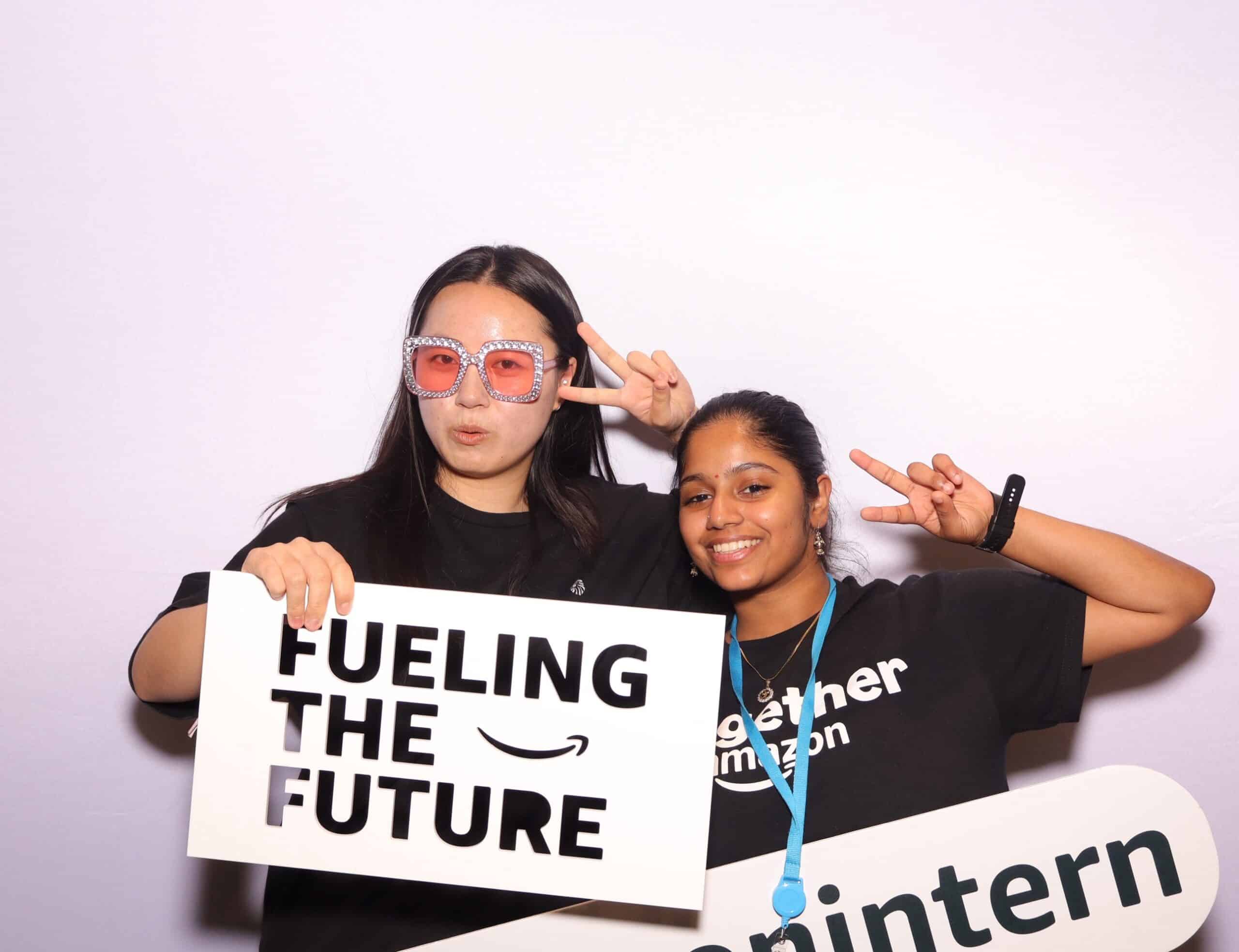 Two young ladies holding a white sign with Amazon logo and the words fueling the future
