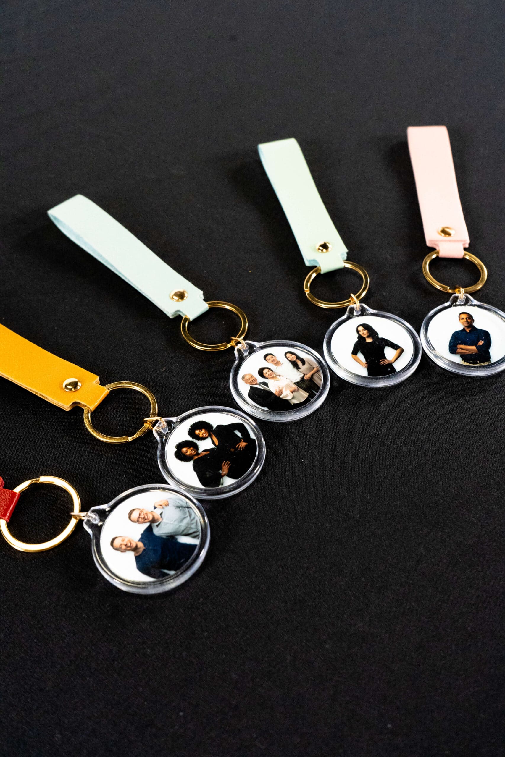 Keychains with circular photo inserts featuring diverse groups of people, showcasing custom photo booth experiences from The Phototique, arranged on a black background.