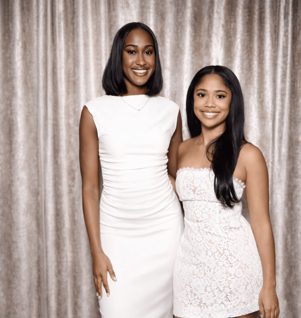 two young ladies standing in front of backdrop curtain white dresses