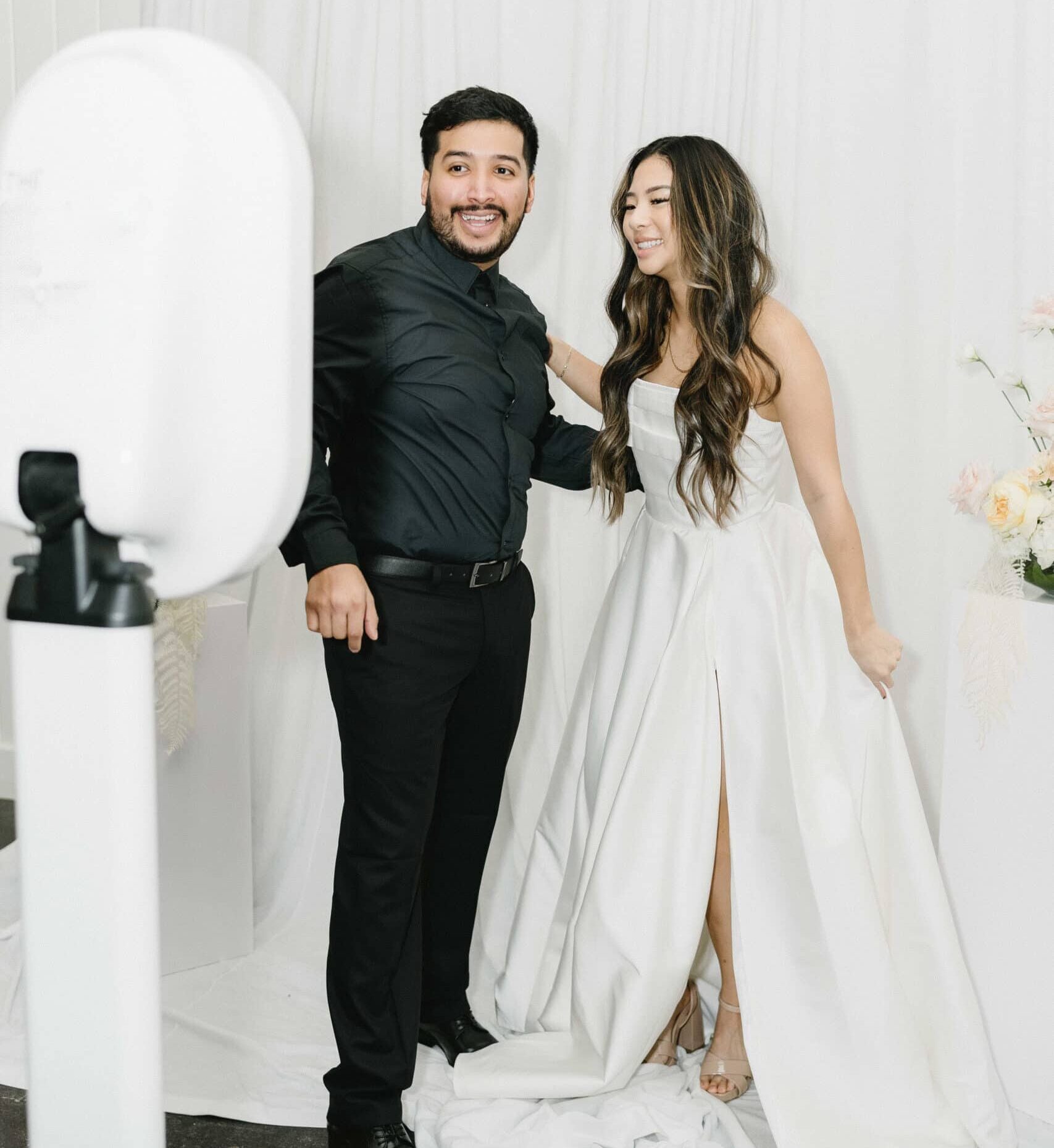 Bride and groom posing for the photo booth in front of luxurious white dreapes