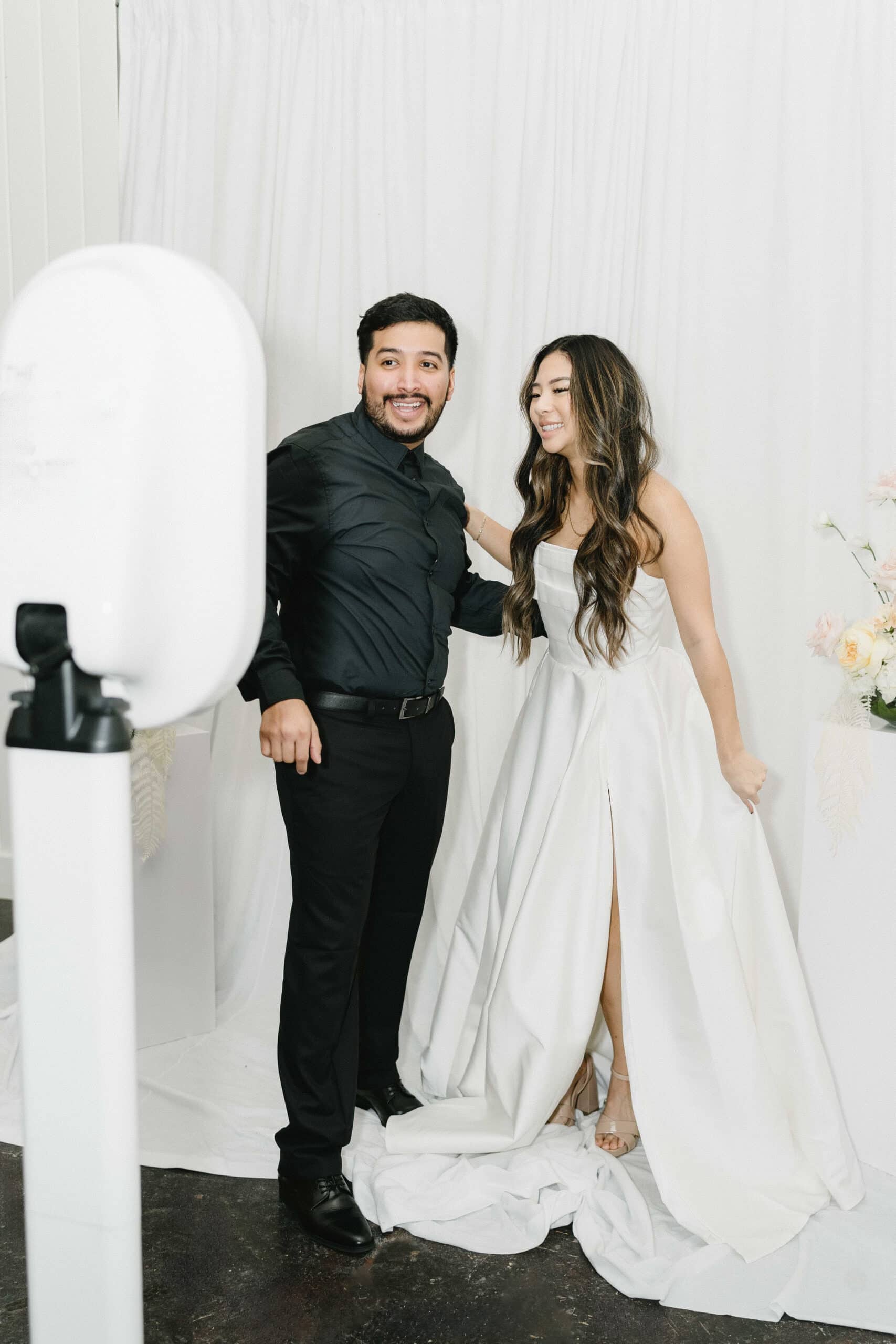 Bride and groom posing for the photo booth in front of luxurious white dreapes