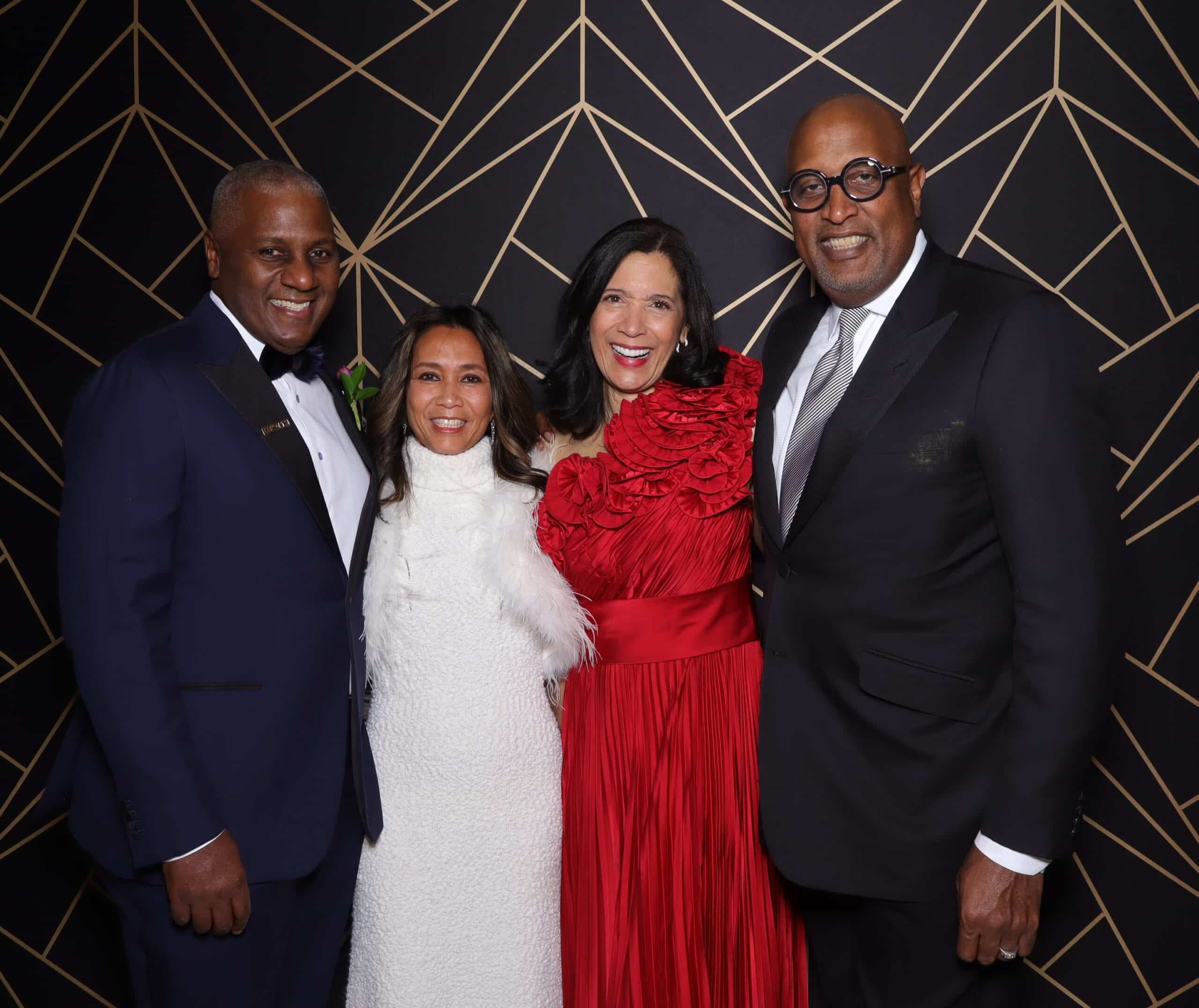 two well dressed couples at a holiday gala posing for the photo booth