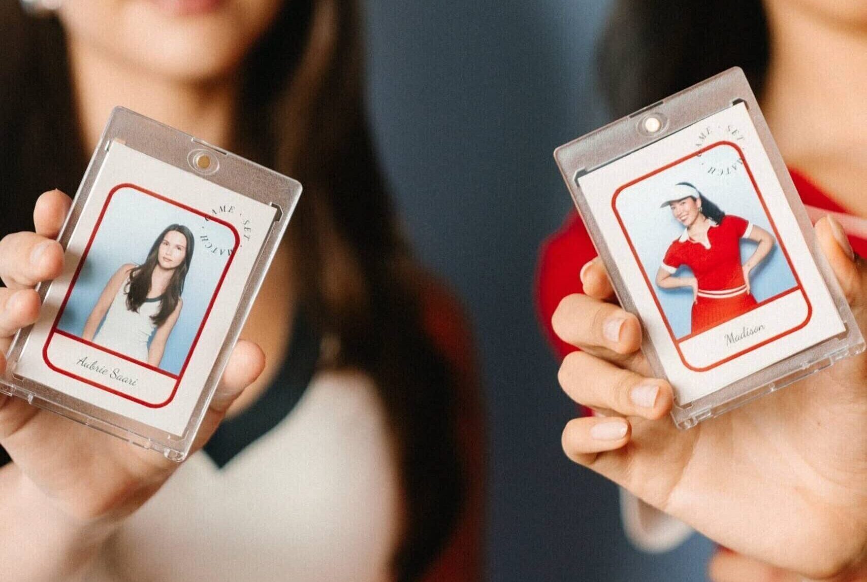 Two women hold up custom trading cards for the camera